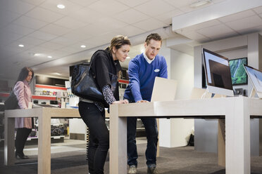 Verkäufer, der einer Kundin beim Kauf eines Laptops im Geschäft hilft - MASF03422