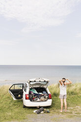 Rückansicht einer Frau, die sich mit einem Auto auf einem Feld gegen das Meer streckt - MASF03428