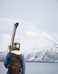 Rückansicht eines Mannes auf Skiern mit Blick auf einen Fluss und schneebedeckte Berge - MASF03429