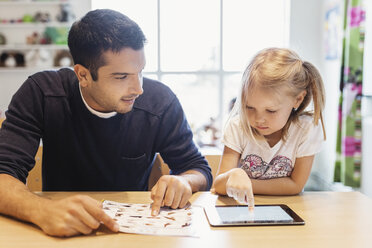 Mid adult male teacher looking at girl using digital tablet at preschool - MASF03447