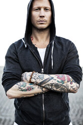 Portrait of a tattooed man in hooded jacket with arms crossed - MASF03462