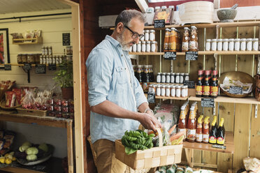 Mature man carrying basket while shopping in food store - MASF03488