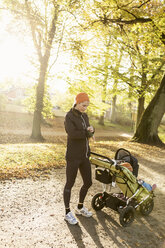 Mutter mit Kinderwagen auf der Straße gegen Bäume im Park - MASF03495