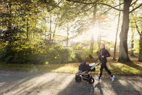 Mutter joggt mit Kinderwagen auf der Straße gegen Bäume im Park - MASF03496