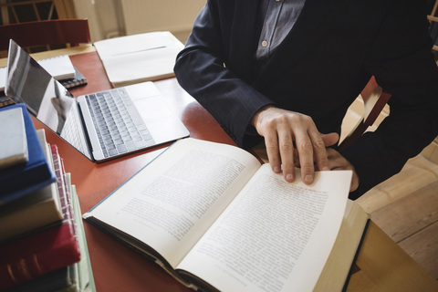 Mittelteil eines männlichen Berufstätigen, der in einer juristischen Bibliothek sitzt und recherchiert, lizenzfreies Stockfoto