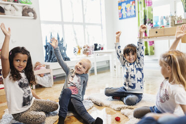 Glückliche Kinder heben die Hände, während sie in der Vorschule sitzen - MASF03510