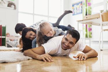 Happy children lying on top of male teacher at preschool - MASF03519