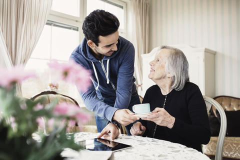 Fröhlicher Pfleger serviert einer älteren Frau im Pflegeheim Kaffee, lizenzfreies Stockfoto