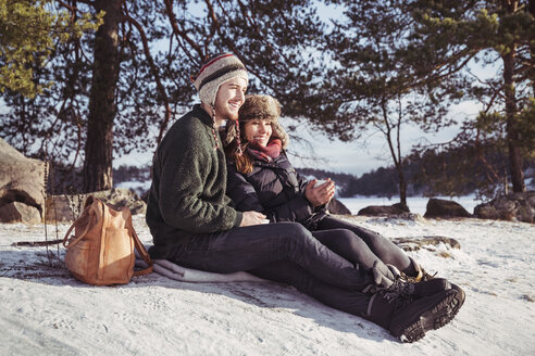 Happy couple enjoying coffee while relaxing on snow covered field - MASF03526