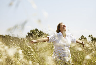Happy mature woman smiling while walking with arms raised in grass field - MASF03535