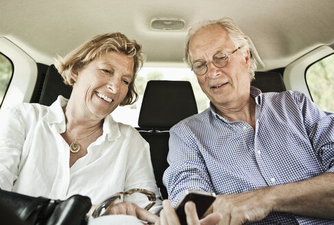 Glückliches Paar, das im Auto sitzend in sein Handy schaut - MASF03536