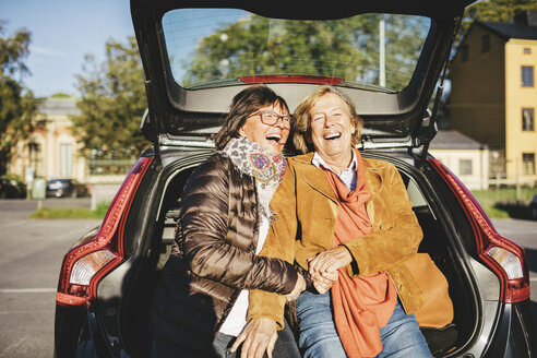 Glückliche ältere Frau sitzt im geöffneten Kofferraum eines Autos - MASF03564