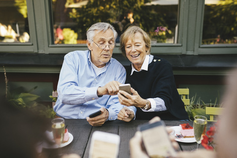 Glückliches älteres Paar, das in einem Restaurant im Freien ein Mobiltelefon benutzt, lizenzfreies Stockfoto