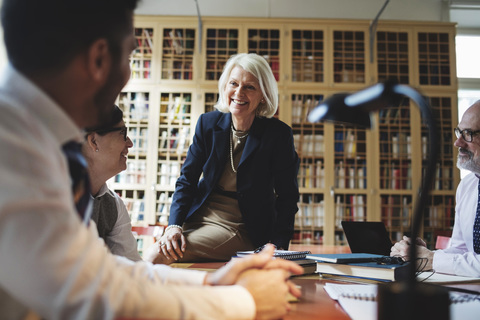 Happy senior lawyer sitting on table during meeting in library stock photo