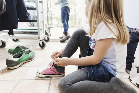 Mädchen trägt Schuh, während sie in der Kindertagesstätte auf dem Boden sitzt, lizenzfreies Stockfoto
