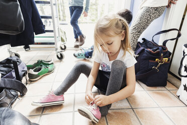 Mädchen trägt Schuh, während sie in der Kindertagesstätte auf dem Boden sitzt - MASF03599