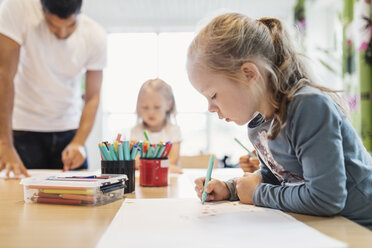 Girl using felt tip pen in drawing class with classmate and teacher in background - MASF03601