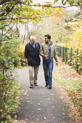 Full length of happy senior man with caretaker walking in park - MASF03602