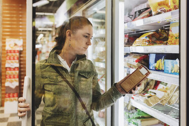 Female customer reading product seen through glass door at refrigerated section - MASF03669