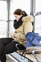 Junge Frau mit Mobiltelefon auf einer Bank am Bahnhof - MASF03672