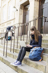 Young woman using laptop on steps of high school - MASF03675