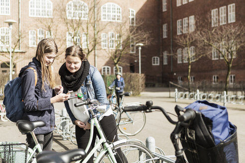 Junge Frauen benutzen ein Mobiltelefon vor dem Schulgebäude - MASF03676