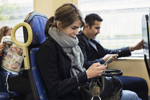 Junge Frau benutzt ein Mobiltelefon, während sie mit einem Mann in der Straßenbahn sitzt - MASF03678