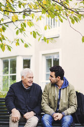 Caretaker communicating with senior man while sitting on bench - MASF03687