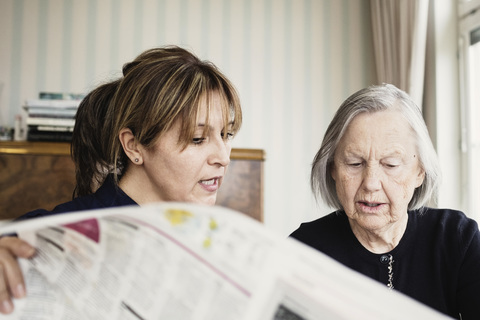 Caretaker with senior woman reading newspaper at nursing home stock photo