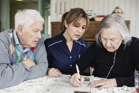 Caretaker assisting senior woman in solving crossword puzzle at nursing home stock photo