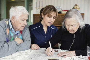 Caretaker assisting senior woman in solving crossword puzzle at nursing home - MASF03692
