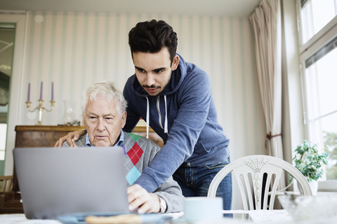 Hausmeister, der einem älteren Mann bei der Benutzung eines Laptops im Pflegeheim hilft, lizenzfreies Stockfoto