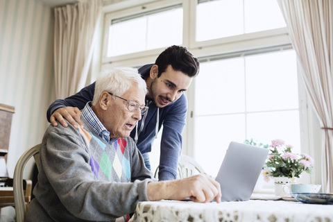 Hausmeister und älterer Mann benutzen Laptop im Pflegeheim, lizenzfreies Stockfoto