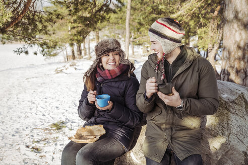 Couple enjoying food while sitting on rock during winter - MASF03702