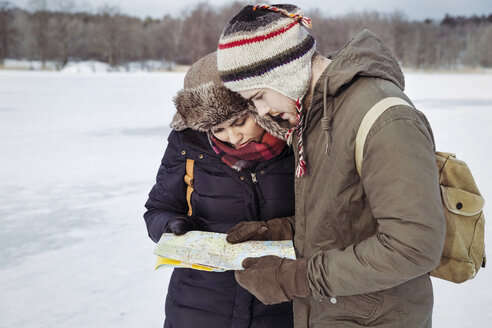 Couple looking at map while standing on field during winter - MASF03704