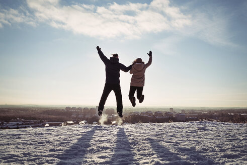 Couple holding hands while jumping on snow covered mountain against sky - MASF03705