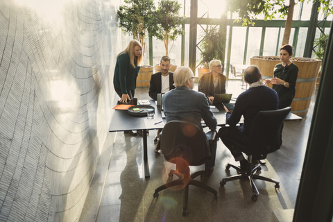 Geschäftsfrau diskutiert mit Kollegen am Tisch in einem kreativen Büro, lizenzfreies Stockfoto