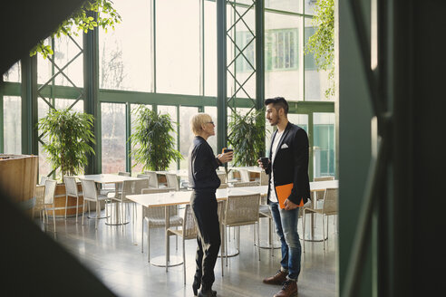 Business people talking while holding coffee cups at office cafeteria - MASF03723