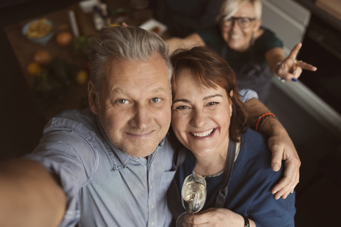 Cheerful mature man with arm around woman while taking selfie in kitchen stock photo