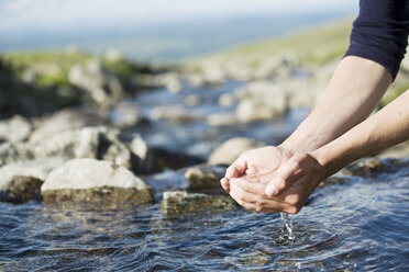 Ausgeschnittenes Bild eines Wanderers, der mit seinen Händen Wasser über einen Bach hält - MASF03746
