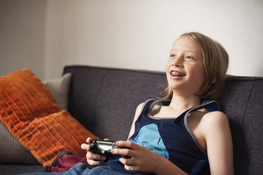 Glücklicher Junge sitzt auf dem Sofa und spielt ein Videospiel - CAVF38009
