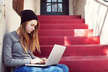 Teenage girl using laptop while sitting on steps outside house - CAVF38017