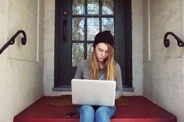Teenager-Mädchen, das einen Laptop benutzt, während es am Hauseingang sitzt - CAVF38019