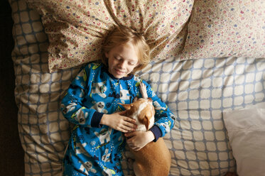 Overhead shot of smiling boy sleeping with dog on bed - CAVF38021