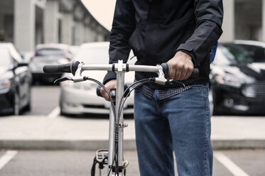 Mittelteil eines Geschäftsmannes, der ein Fahrrad auf einer Straße in der Stadt hält - CAVF38045