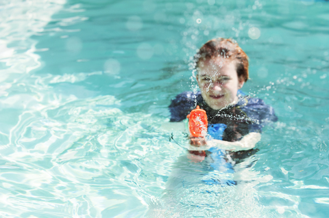 Porträt eines Teenagers, der mit einer Wasserpistole im Schwimmbad spielt, lizenzfreies Stockfoto