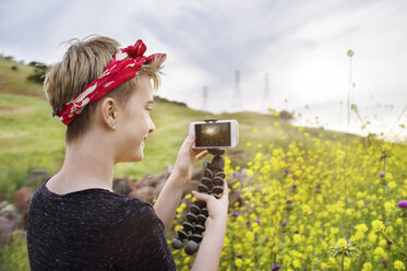 Rückansicht eines glücklichen Teenager-Mädchens, das mit seinem Smartphone ein Feld gegen den Himmel fotografiert - CAVF38096