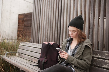 Young woman using smart phone while sitting on bench - CAVF38103