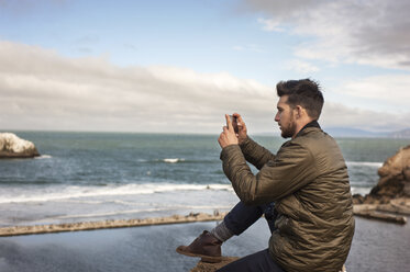 Seitenansicht eines Mannes, der mit seinem Smartphone das Meer gegen den Himmel fotografiert - CAVF38115