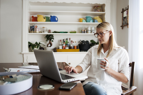 Frau mit Laptop und Becher in der Hand zu Hause, lizenzfreies Stockfoto